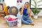 Young beautiful woman doing laundry sitting by wicker basket showing and pointing up with fingers number four while smiling