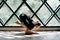 Young beautiful woman doing yoga asana baby crow pose on triangular window background