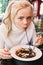 Young beautiful woman eating black pasta with seafood and cuttlefish ink in the outdoor restaurant. Funny and beautiful.