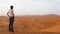 Young beautiful woman enjoying an amazing view over the red dunes sea of Erg Chebbi, with camel bedouins on background, Morocco.