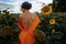 Young Beautiful Woman in evening dress In A Field Of Sunflowers Stands Back, Rear View, Sunset