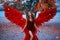 Young beautiful woman fallen angel stands in the park near a tree with orange falling leaves. Creative red suit, huge