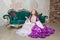 Young beautiful woman in fantasy white and purple rococo style medieval dress sitting near sofa and praying