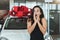 Young beautiful woman feels surprised receiving brand new car for present in dealership center