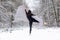 Young beautiful woman girl ballerina with long hair in black ballet suit jumps and dances on toe peak in snowy winter forest