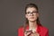 Young beautiful woman with glasses looks up thoughtfully, holding a phone in her hands. Gray background