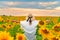 Young beautiful woman in hat rise hands to the susnet with clouds and field of sunflowers.