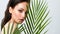 Young beautiful woman with healthy skin of face and palm leaves. Closeup fresh face of an attractive caucasian girl with green