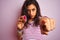 Young beautiful woman holding amethyst gemstone over isolated pink background pointing with finger to the camera and to you, hand