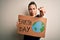 Young beautiful woman holding banner asking for earth and enviroment conservation pointing with finger to the camera and to you,