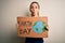 Young beautiful woman holding banner asking for earth and enviroment conservation scared in shock with a surprise face, afraid and