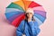 Young beautiful woman holding colorful umbrella covering mouth with hand, shocked and afraid for mistake