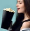 Young beautiful woman holding eating popcorn over mint background