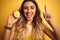 Young beautiful woman holding half lemon over yellow isolated background surprised with an idea or question pointing finger with