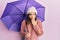 Young beautiful woman holding purple umbrella covering mouth with hand, shocked and afraid for mistake
