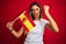 Young beautiful woman holding spanish flag over red isolated background annoyed and frustrated shouting with anger, crazy and