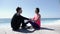 Young beautiful woman kisses fit sportive man in the lips on the beach while sitting. Slow motion