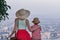 Young beautiful woman in large straw hat hugge little boy and look at the panorama of city. Back view