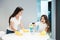 Young beautiful woman laughing while her cute teen daughter spraying detergent to wipe dust off the table