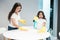Young beautiful woman laughing while her cute teen daughter spraying detergent to wipe dust off the table while cleaning