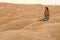 Young beautiful woman with long hair in blue dress sitting elegant and thoughtful on sand at sunrise in sandy desert