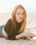 Young beautiful woman with long hair is relaxing on sandy beach with mobile phone in backlight.