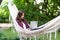 Young beautiful woman lying in a hammock with laptop in a garden. green background. Trees. telework. remote work