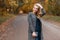 Young beautiful woman model in gray trendy coat in a vintage blouse with a handbag stands in a park on the road