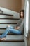 Young beautiful woman model with messy long hair in ripped blue jeans and striped t-shirt sitting indoor by window