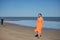 Young and beautiful woman in an orange dress and pink heels in her hand, walking barefoot on the beach in solitude. Concept beauty
