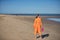 Young and beautiful woman in an orange dress and pink heels in her hand, walking barefoot on the beach in solitude. Concept beauty