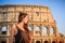 Young beautiful woman posing in front of the Colosseum. Marble arches ruins over a blue sky, Rome, Italy