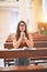 Young beautiful woman praying on her knees in a bench at church