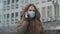 Young beautiful woman in protective mask standing in city and talking on the phone. Ill brunette girl coughing. Global