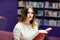 Young beautiful woman in public library, holding, reading and choosing books for leisure or education. Woman making