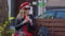 Young beautiful woman in a red beret and dress, black glasses and a braid is sitting on a park bench with cup of coffee