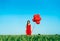 Young beautiful woman in red dress posing in green field with red balloons