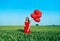 Young beautiful woman in red dress posing in green field with red balloons