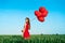 Young beautiful woman in red dress posing in green field with red balloons