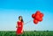 Young beautiful woman in red dress posing in green field with red balloons