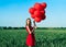 Young beautiful woman in red dress posing in green field with red balloons