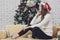 Young beautiful woman in red hat sitting on sofa between christmas trees and listening to music with headphone in front of hugh c