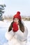 Young beautiful woman in red knitted hat and mittens warms her hands in winter outdoors. Snowy day