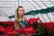 Young beautiful woman in a shawl among red flowers in a greenhouse with poinsettias holds one of the flowers in her hands