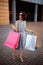 Young beautiful woman shopaholic walks out the shopping center with a pack of bags with purchases. Pink shopper in the hand of an