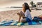 Young beautiful woman sits on the sand of a beach with a smartphone in her hands during sunset