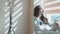 A young beautiful woman sits on a window overlooking the sea. On the table is a vase with decorative flowers. The rays