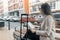 Young beautiful woman sitting on bench with travel suitcase and reading city map, drinks coffee, city street background