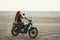 Young beautiful woman sitting on her old cafe racer motorcycle in desert at sunset or sunrise