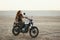 Young beautiful woman sitting on her old cafe racer motorcycle in desert at sunset or sunrise